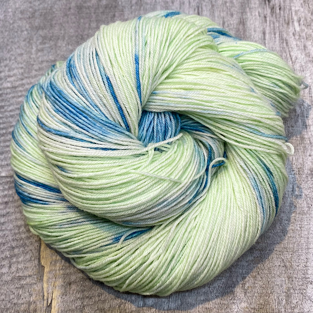 A swirl of hand dyed wool in colour, 'East Beach'. A pale green/yellow background with blue dye painted through.